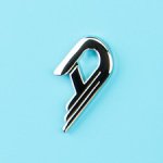 Duesenberg logo in a sleek silver finish, shaped as a stylized letter 'D' with three parallel lines extending from its lower curve. The emblem is set against a Narvik Blue background, highlighting its metallic elegance and modern craftsmanship.