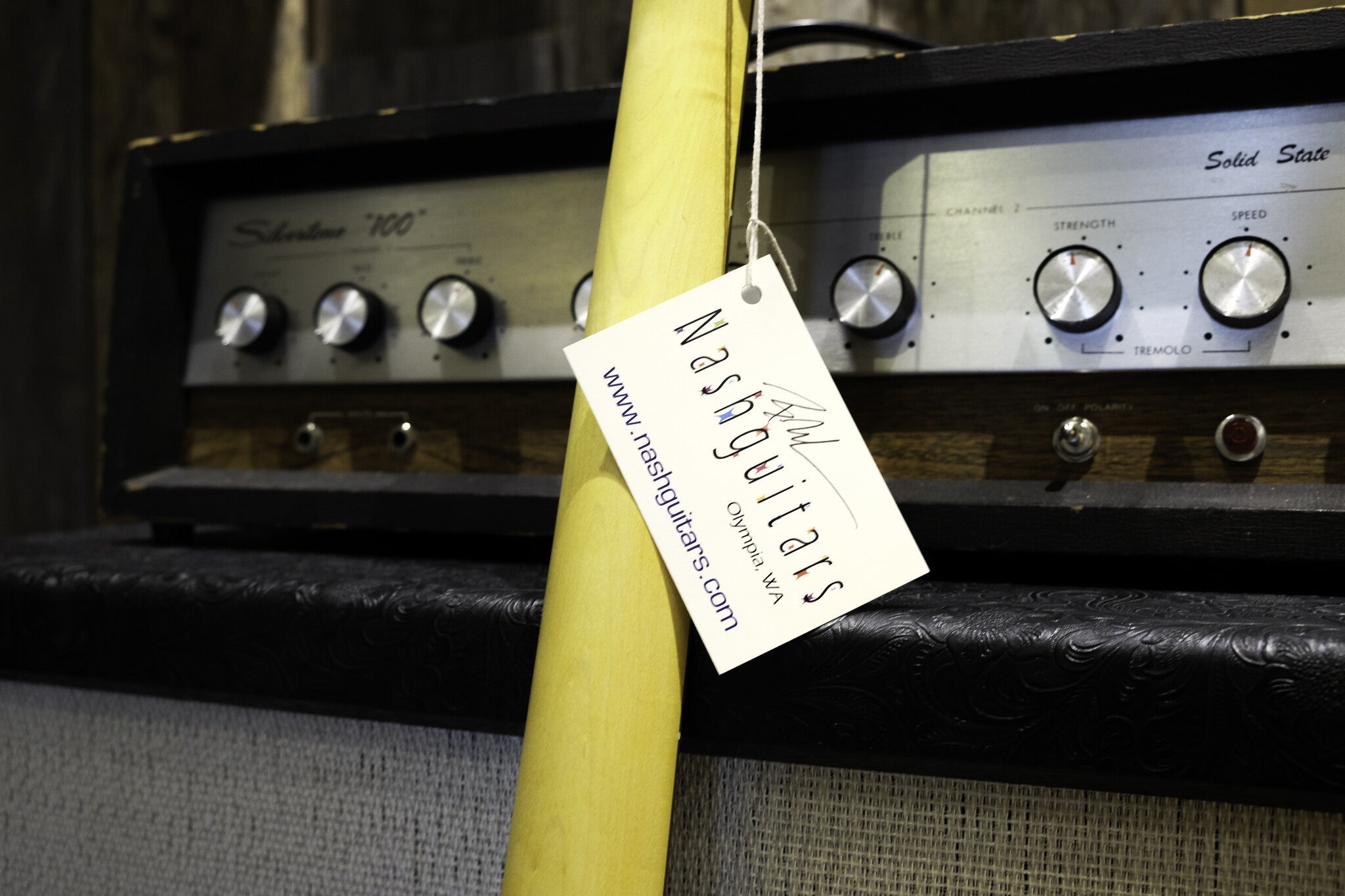 Close-up of a Nash guitar neck with a tag attached, displaying 'Nashguitars' branding and website details.