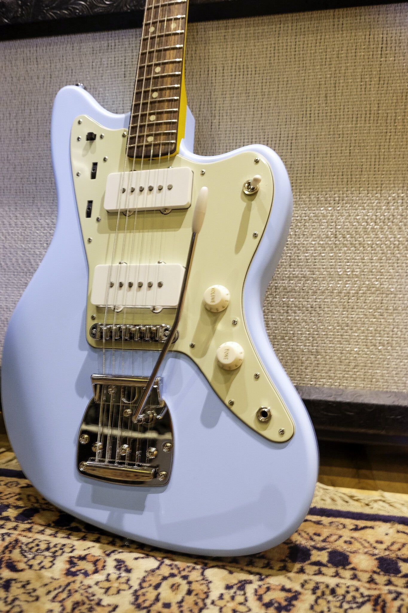 Vintage-style electric Nash guitar in Sonic blue and light green resting against a textured amplifier.