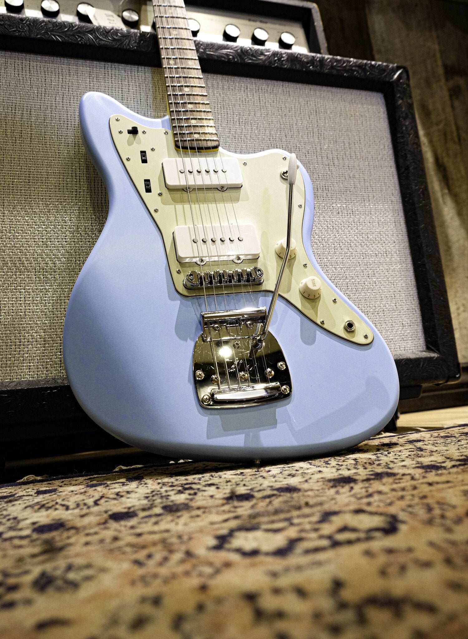 Retro sonic blue and light green guitar with a classic tremolo bridge, paired with an amp and drum set in a music studio.