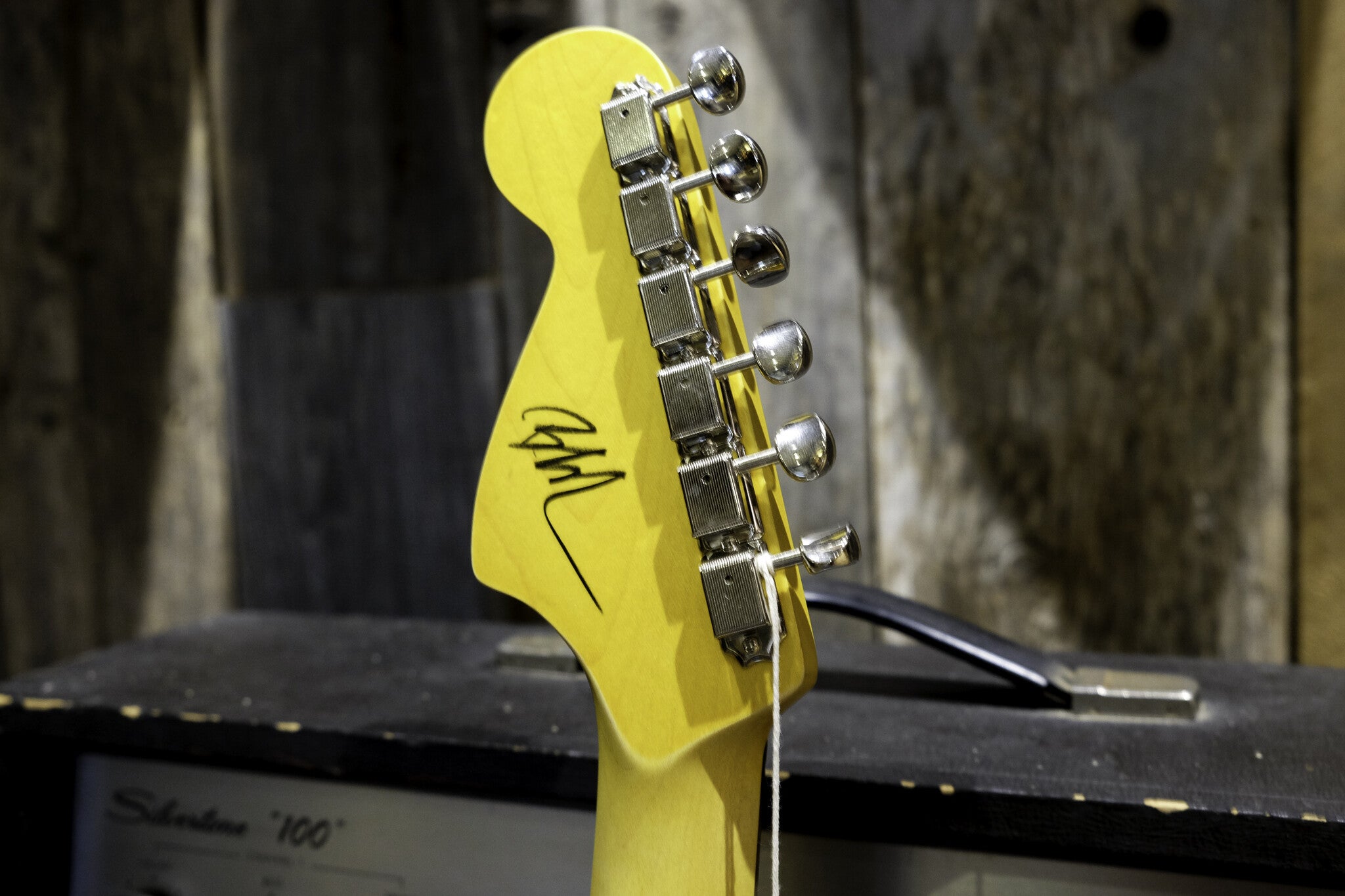 Yellow Nash guitar headstock with six metallic tuning pegs, featuring a black ink signature.