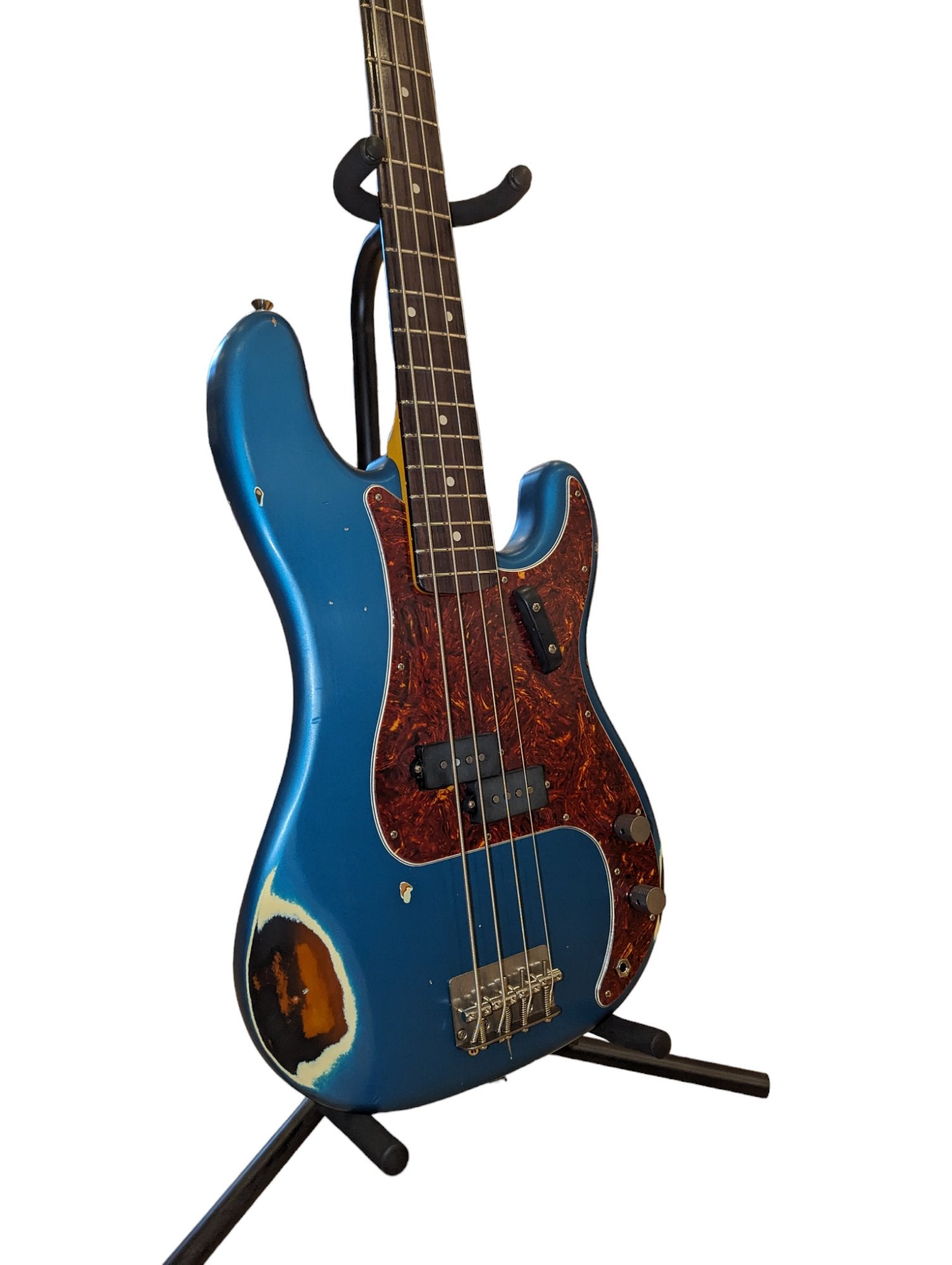 Blue Nash bass guitar with a tortoiseshell pickguard, visible wear on the body exposing natural wood, standing on a black guitar stand.