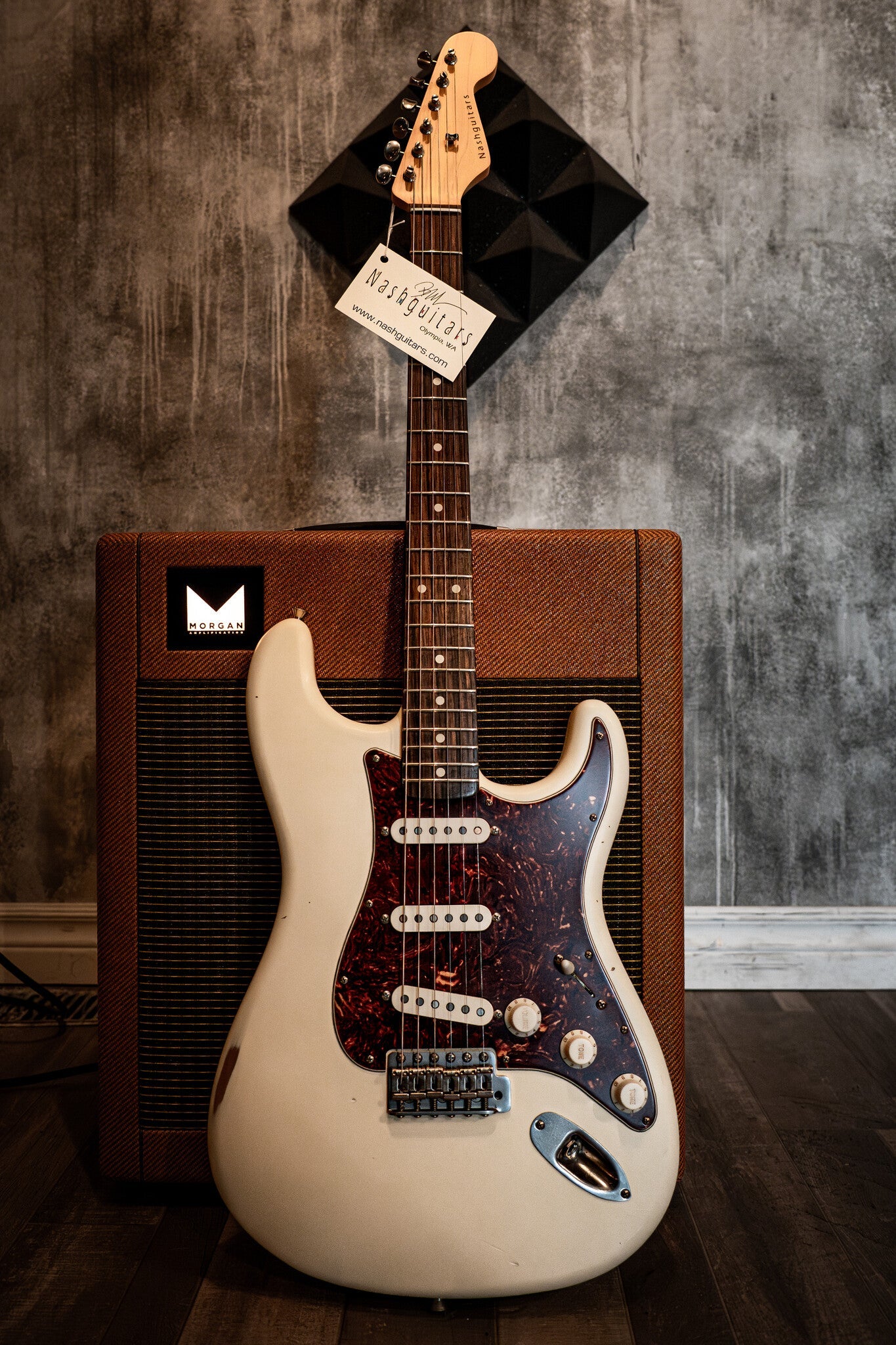 Cream-colored Nash electric guitar with a tortoiseshell pickguard, leaning against a brown Morgan Amplification amp.