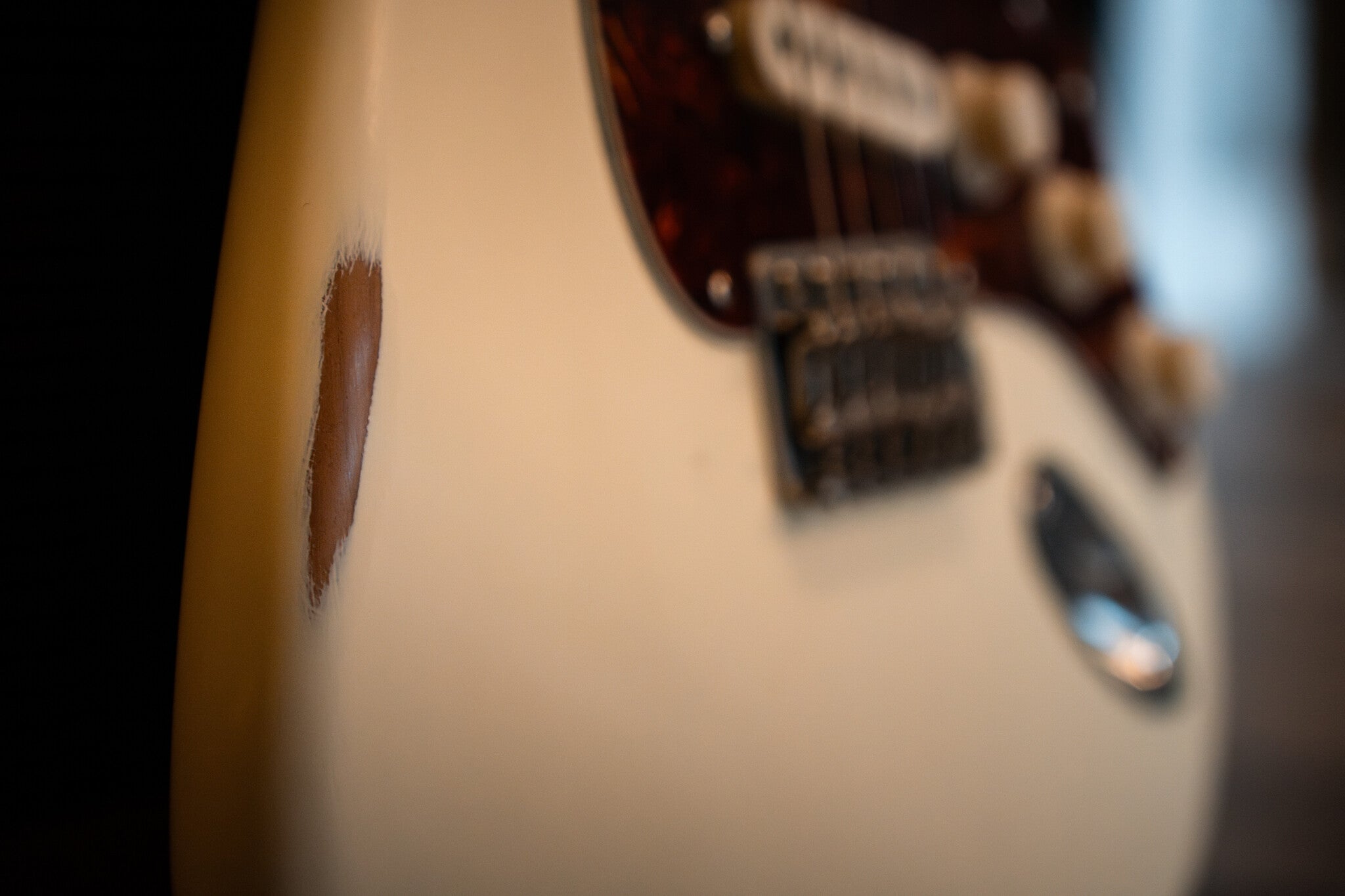 Close-up of a white Nash electric guitar with a chipped body, revealing natural wood beneath the paint