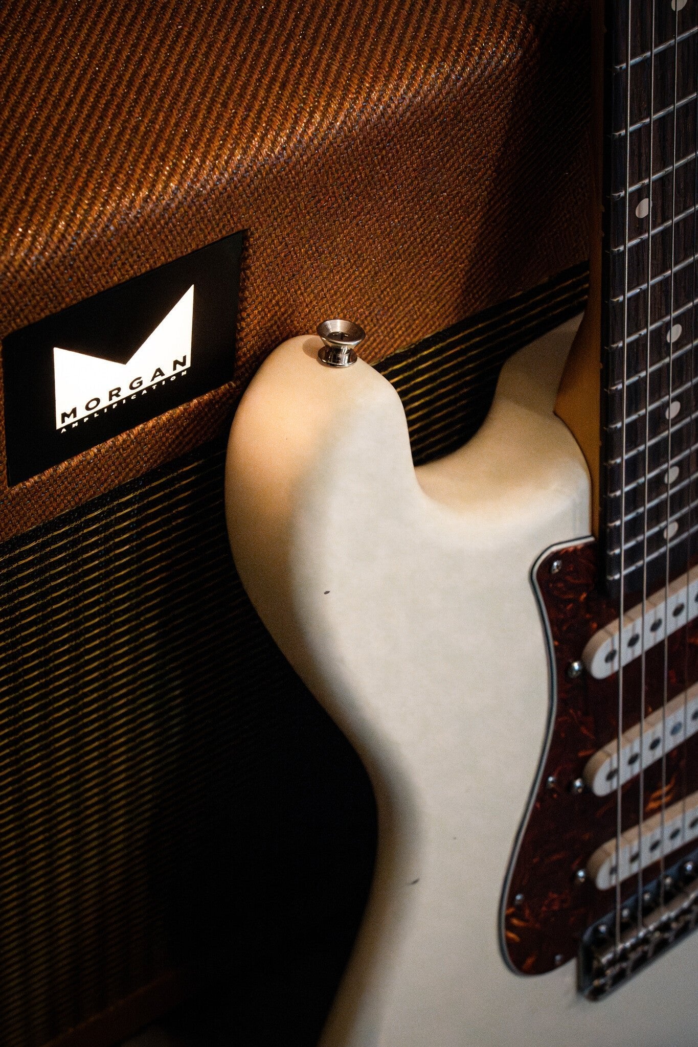 Cream-colored Nash electric guitar with a tortoiseshell pickguard, leaning against a brown Morgan Amplification amp with a textured front panel and white lettering.
